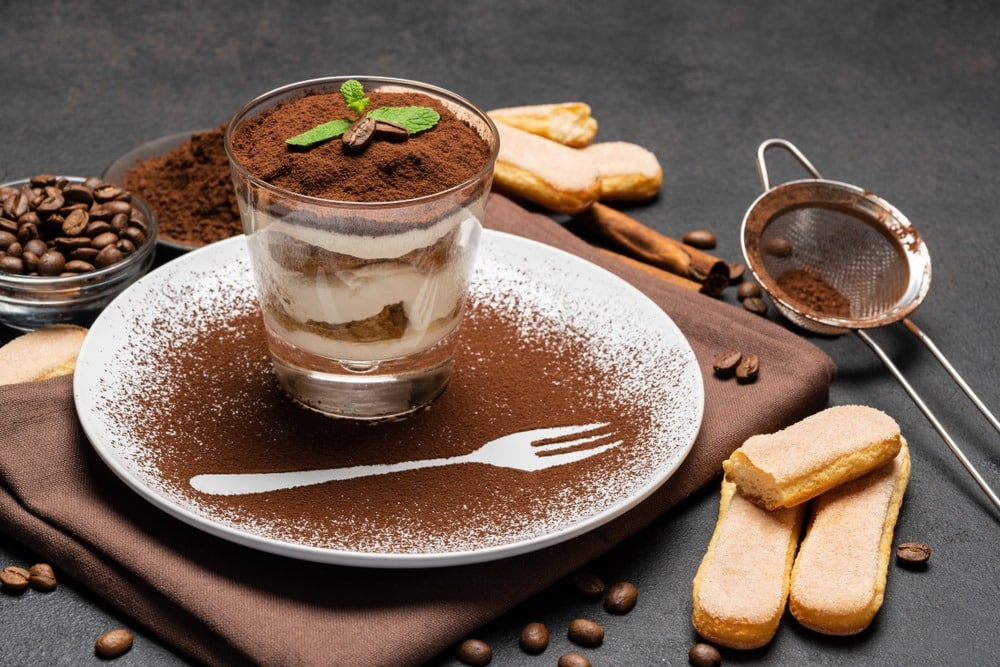 Classic tiramisu dessert in a glass and cup of coffee on dark concrete background