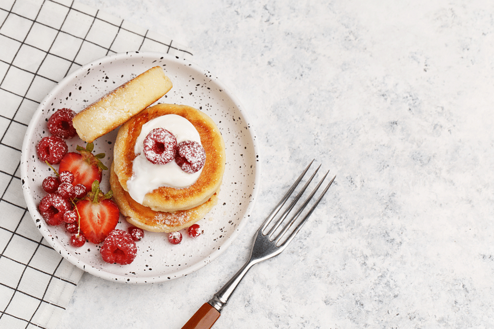 Cottage cheese pancakes with sour cream and fresh berries on white marble background