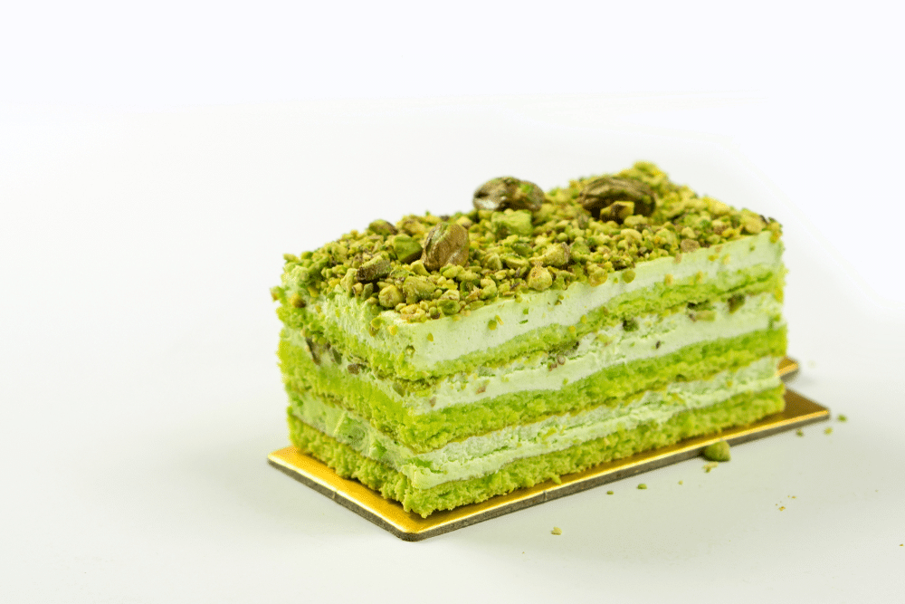 Green Sicilian Pistachio Cake slice with vanilla almond and nuts toppings in white background