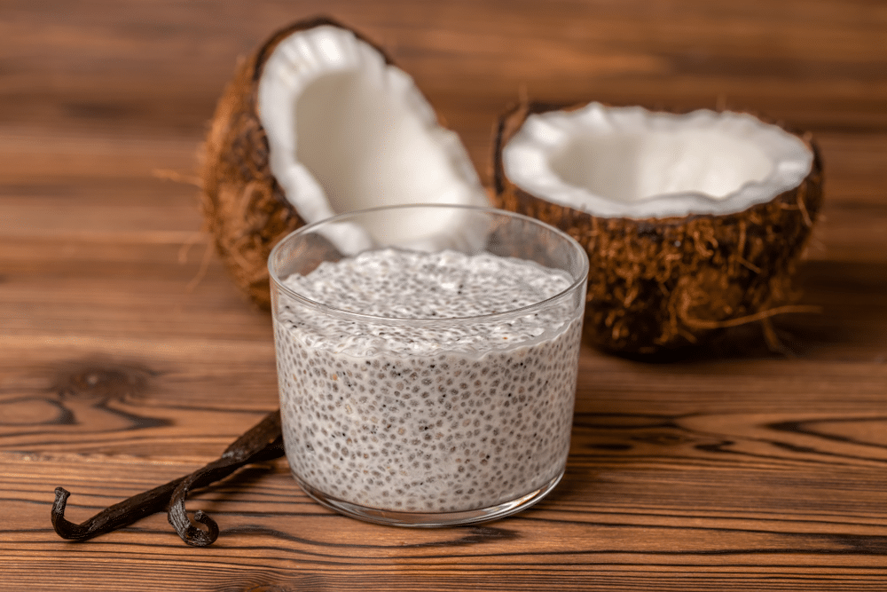 chia pudding in glass decorated vanilla pods and coconuts on wooden background