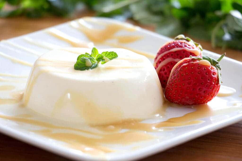 Panna Cotta served in a plate along with condense milk and strawberries