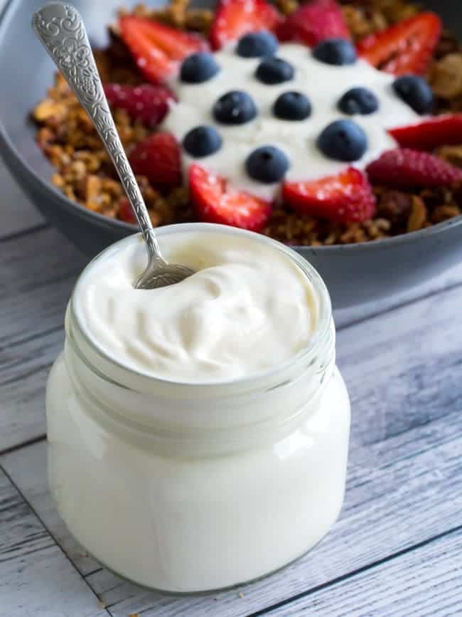 a jar of keto yougurt along with the bowl of cereal with strawberry and blueberry