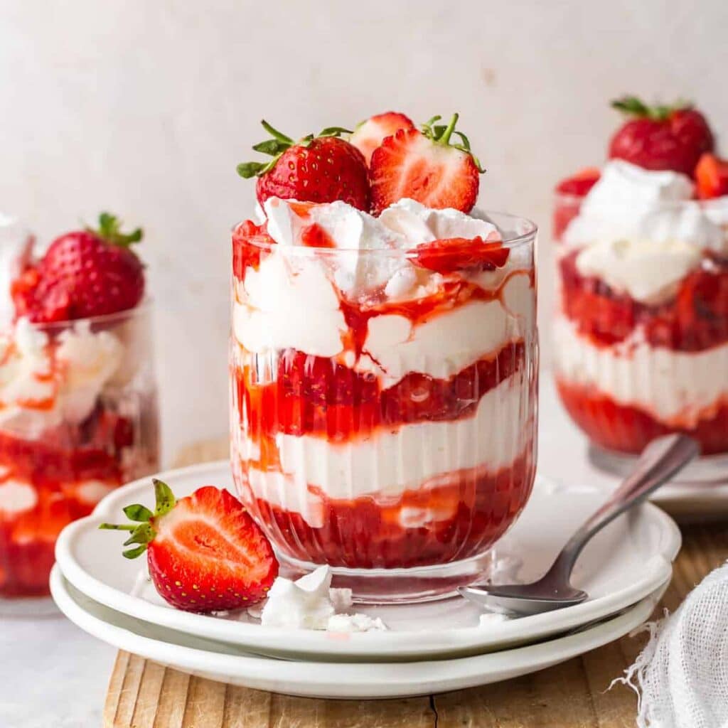 A view of strawberry eton mess served in a glass bowl with strawberries on the side