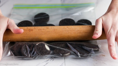 A view of a person crushing oreos with a rolling pin inside a plastic bag