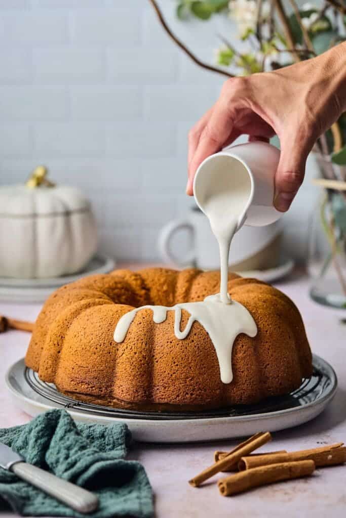 A view of a person pouring cream on a bundt cake with pumpkin