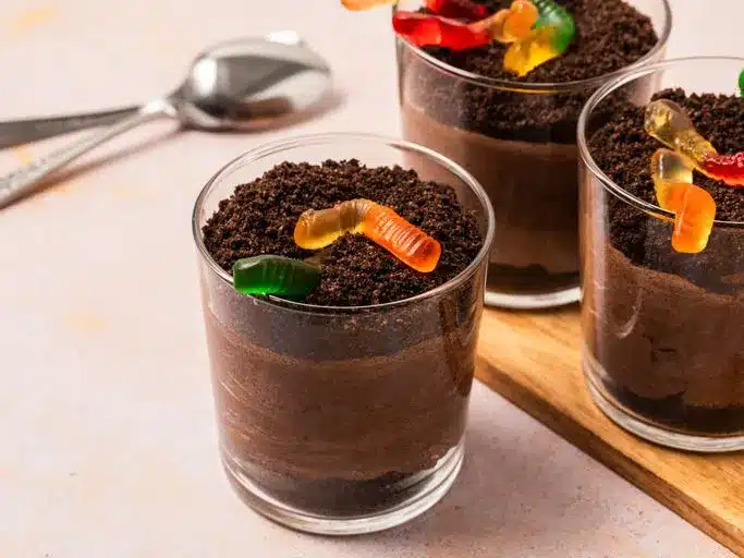 A view of three glass cups filled with dirt dessert topped with gummy worms