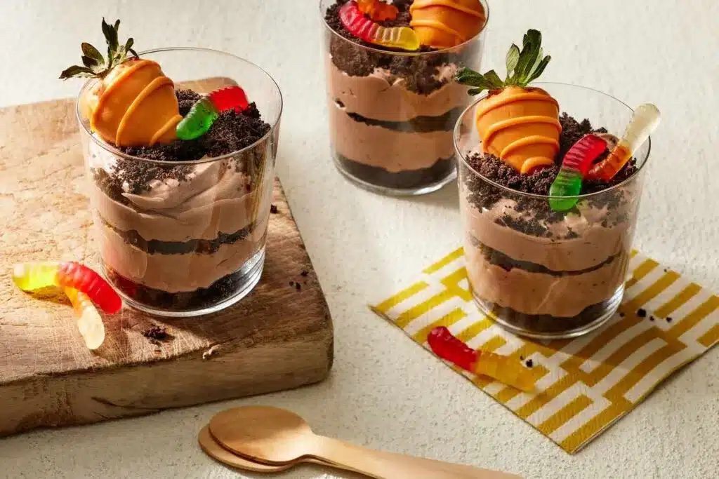 A view of three glass cups filled with dirt dessert topped with gummy worms