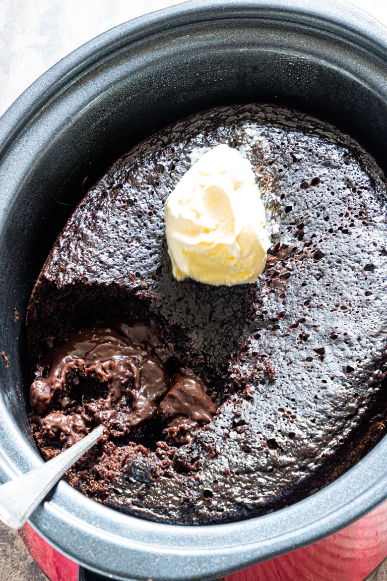 An overhead view of a chocolate cake inside a crockpot with ice cream on top