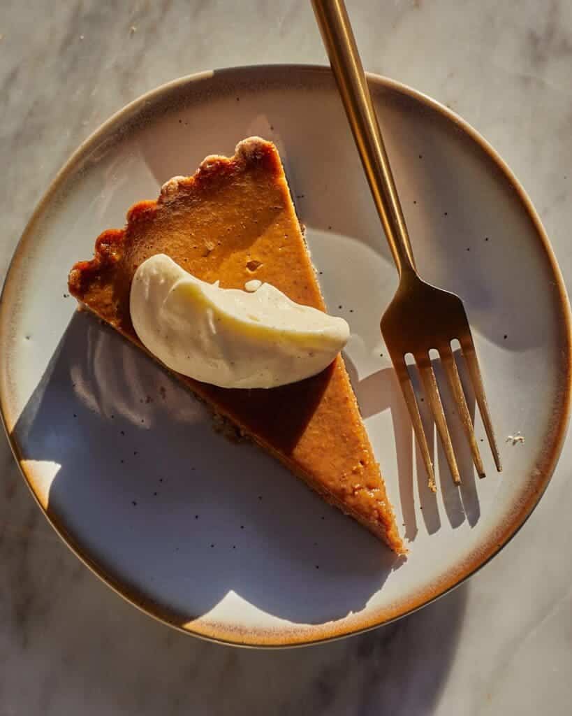 An overhead view of a slice of spiced pie tart with a fork and cream topping