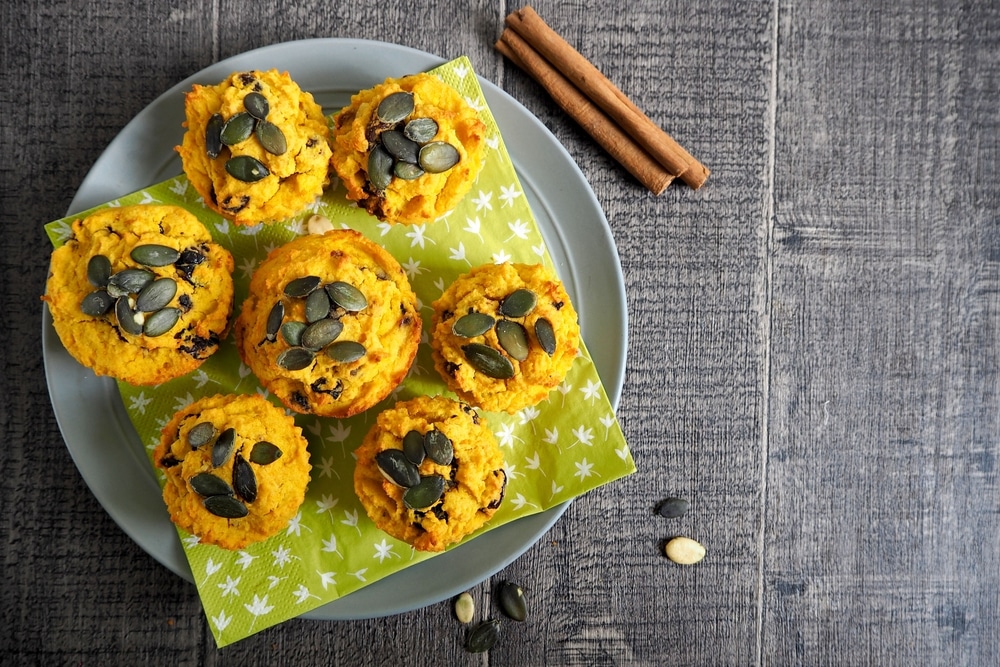 gluten-free pumpkin cupcakes, sprinkled with pumpkin seeds, lie side by side on a green napkin on a wooden table