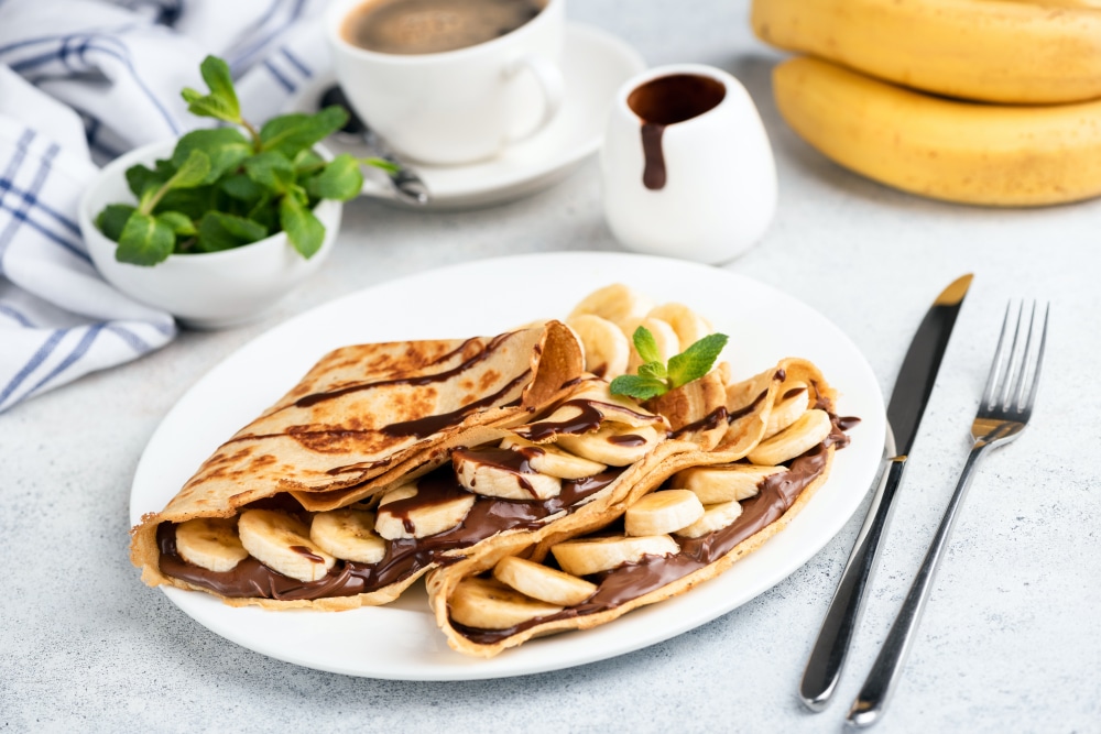 French crepes with nutella spread and banana on white plate