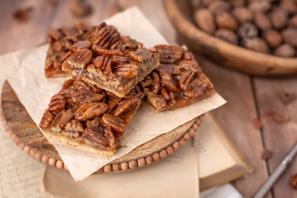 Close up Of Homemade Pecan Bars On Pedestal With Bowl Of